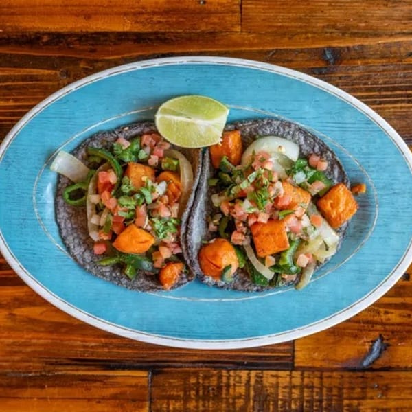 Two vibrant tacos with sweet potato, peppers, and pico de gallo on blue corn tortillas, garnished with lime.