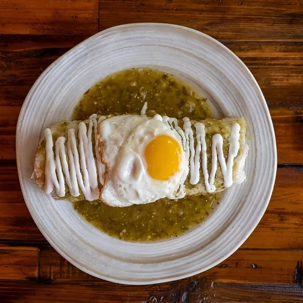Burrito covered in green sauce, drizzled with white cream, and topped with a fried egg.