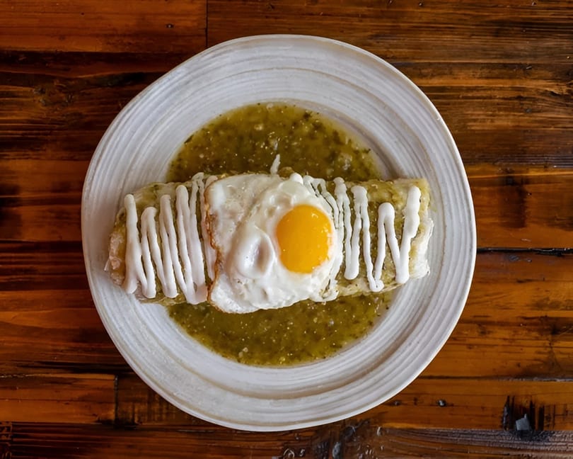 Burrito covered in green sauce, drizzled with white cream, and topped with a fried egg.