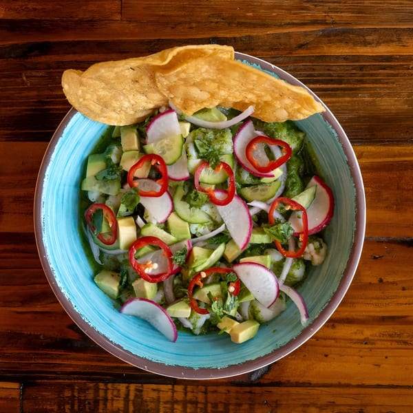 Overhead view of a vibrant ceviche dish with avocado, radishes, and red peppers in a blue bowl.
