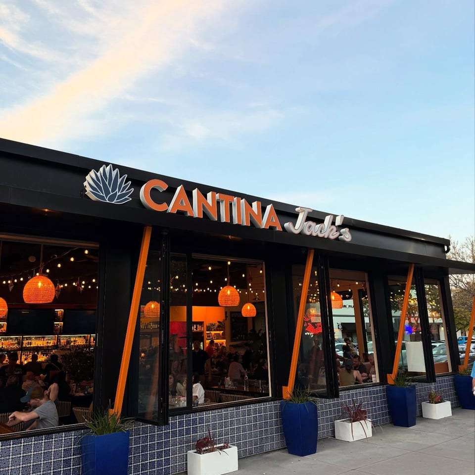 Cantina Jack’s restaurant exterior with orange signage, tiled facade, glowing pendant lights, and diners visible through windows.