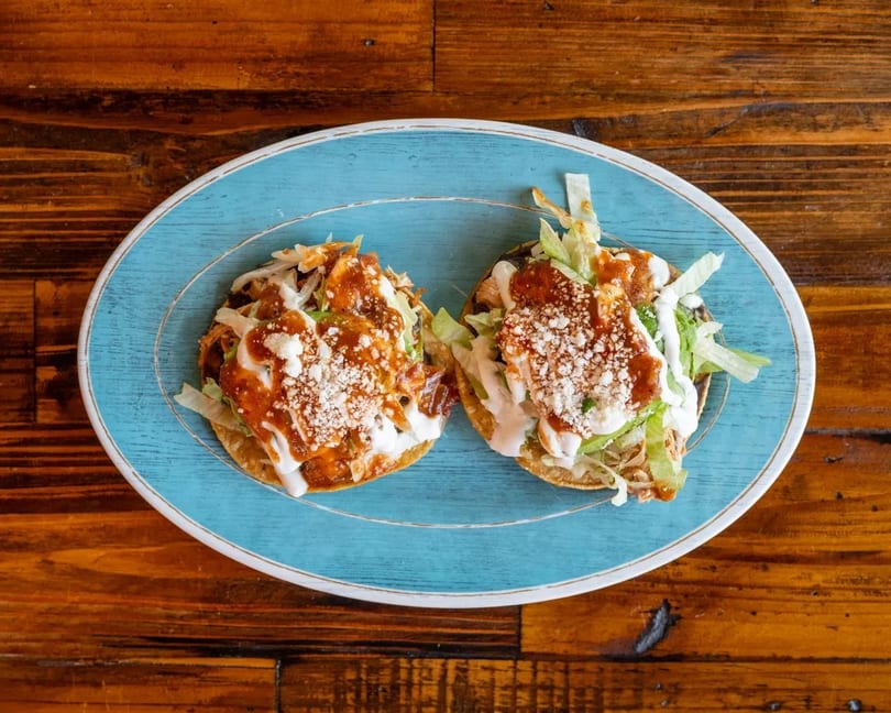 Two tostadas topped with meat, lettuce, sauce, and crumbled cheese on a blue plate.