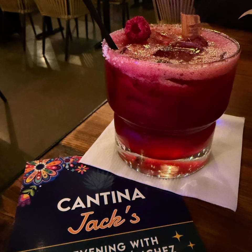 Red cocktail garnished with a raspberry and gold sugar rim sits on a table at Cantina Jack’s restaurant.