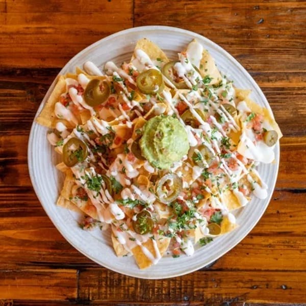 A plate of nachos with guacamole, jalapeños, pico de gallo, and a white sauce drizzle.
