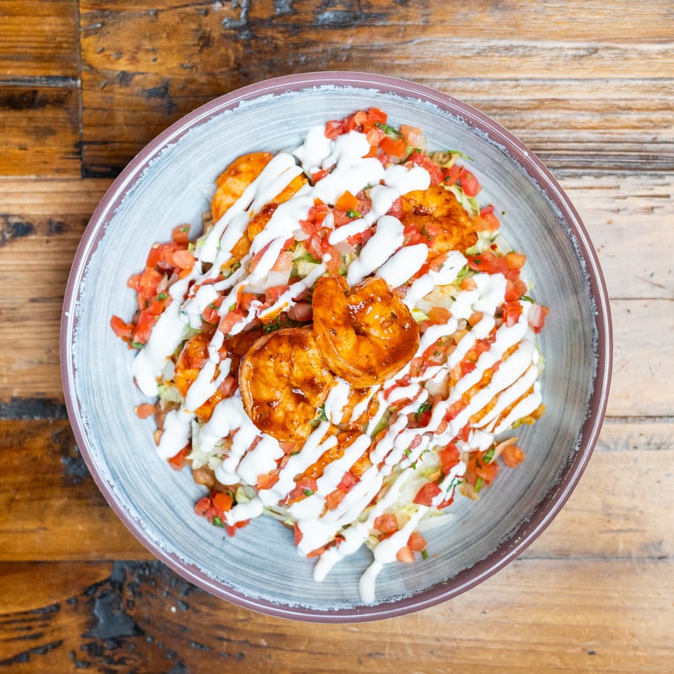 Overhead view of grilled shrimp salad with lettuce, diced tomatoes, and creamy white dressing on a rustic wooden table.