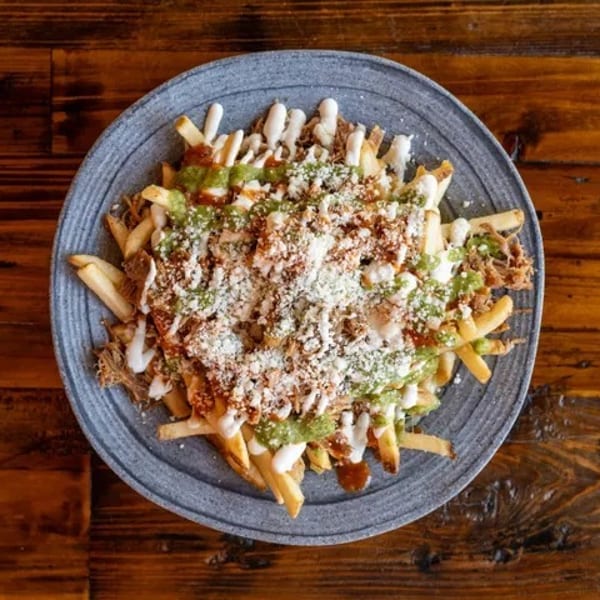 Loaded fries topped with green sauce, white sauce, shredded meat, and cheese on a gray plate.