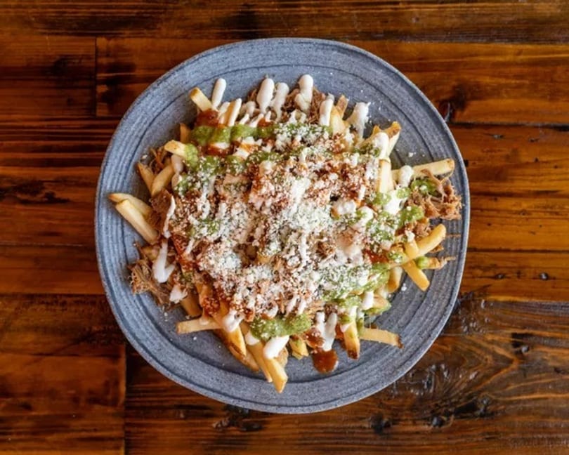 Loaded fries topped with green sauce, white sauce, shredded meat, and cheese on a gray plate.
