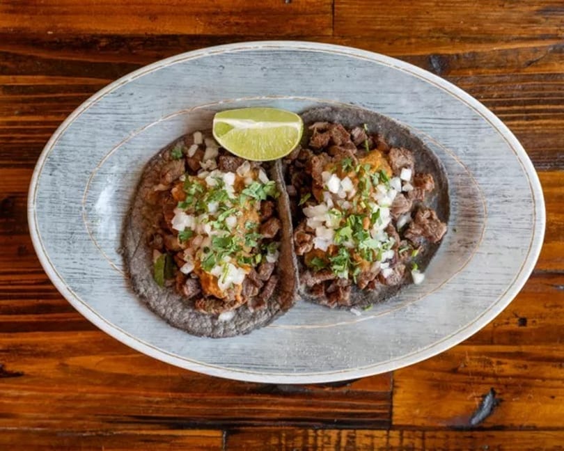 Two street tacos with meat, onions, cilantro, and salsa, served with a lime wedge on a plate.