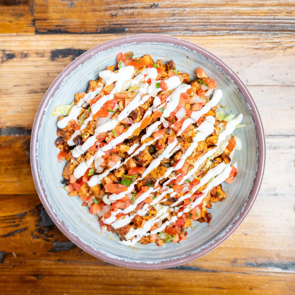 Overhead view of a plate piled with grilled chicken, diced tomatoes, lettuce, herbs, and creamy white sauce on a wooden table.