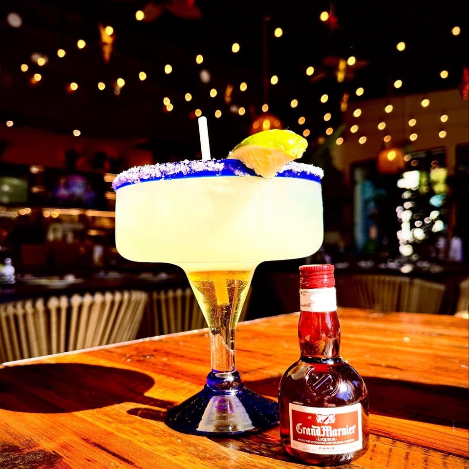 Margarita with a salt rim and lime garnish beside a Grand Marnier bottle on a warmly lit restaurant bar.