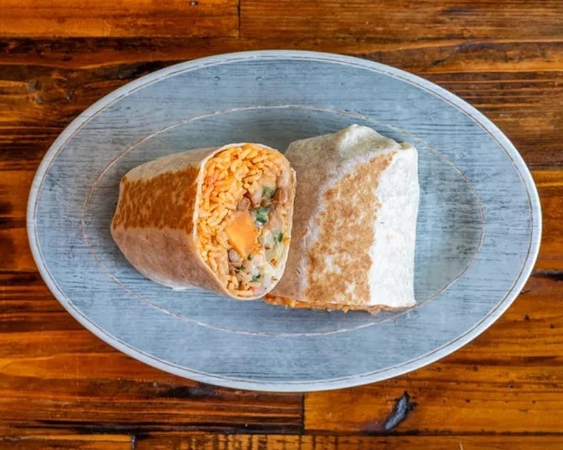 Two burritos, one cut open to reveal rice, beans, and vegetables, on a blue plate.