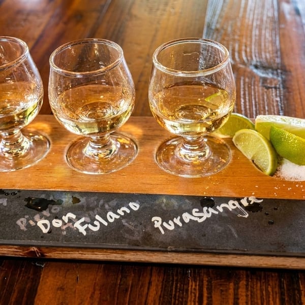 Three tequila shots with lime wedges and salt on a wooden serving board.