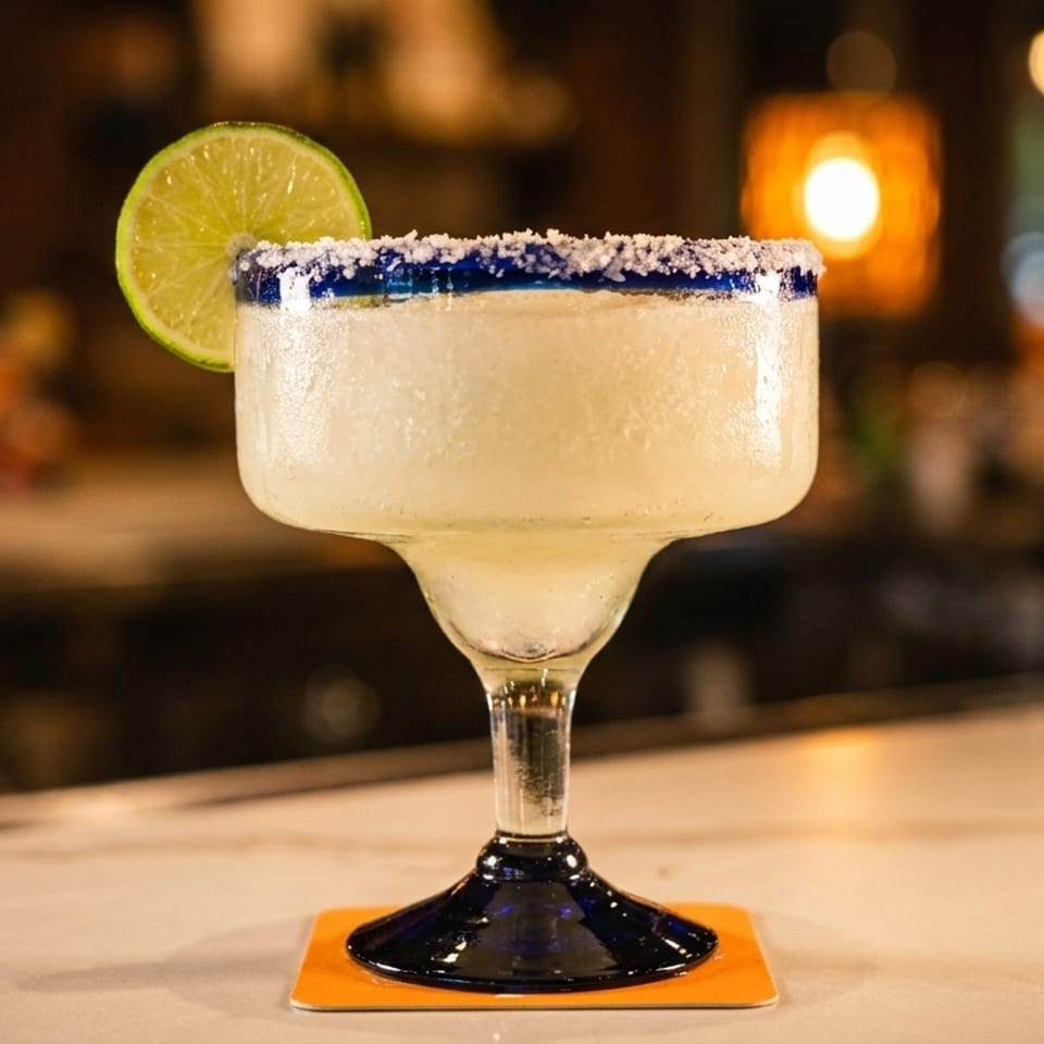 A frozen margarita with a salted rim and lime wedge sits on a bar.